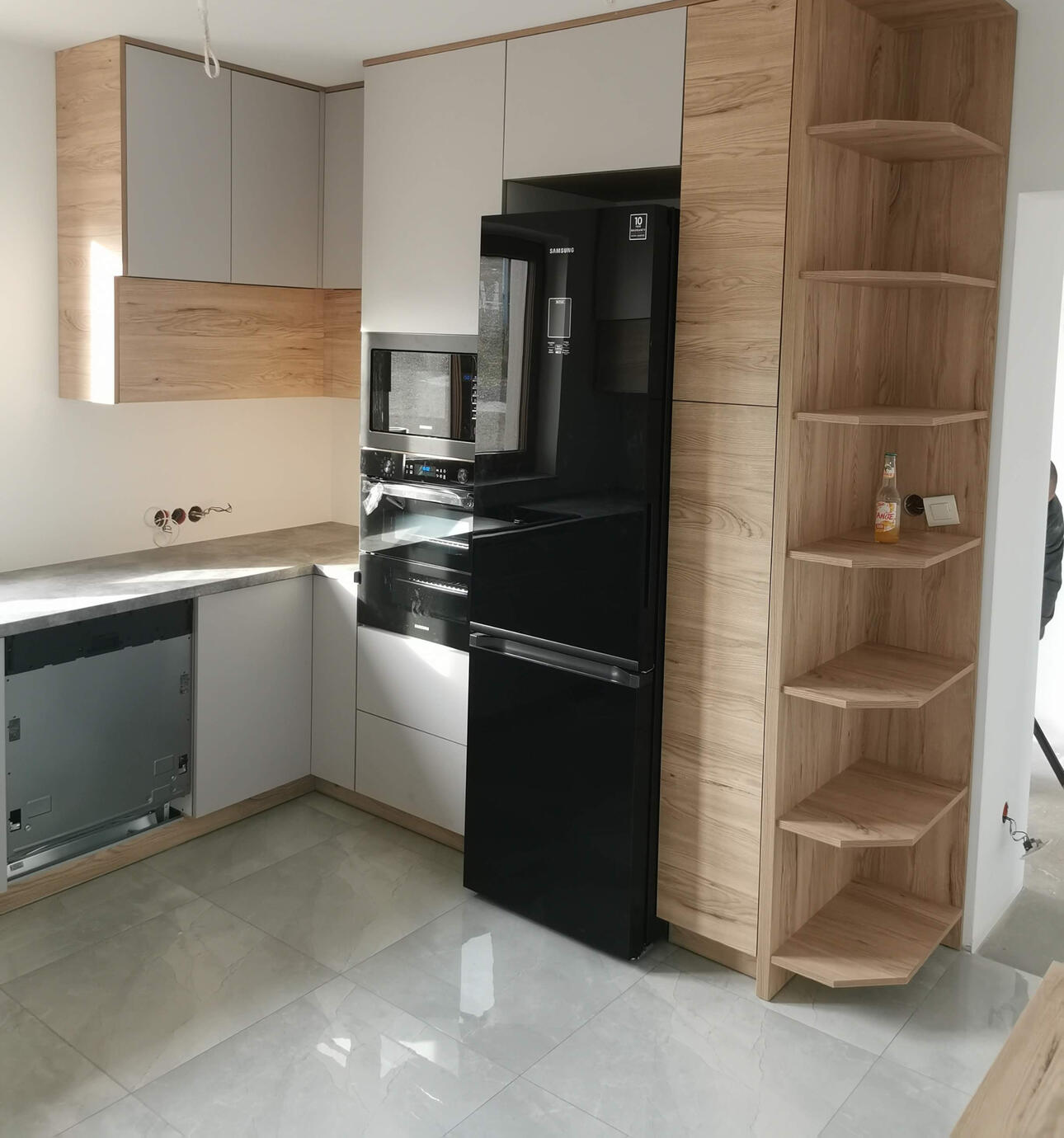 Jasne, matowe fronty szafek i szuflad kontrastują z ciepłymi akcentami drewna, które przywołują atmosferę natury.