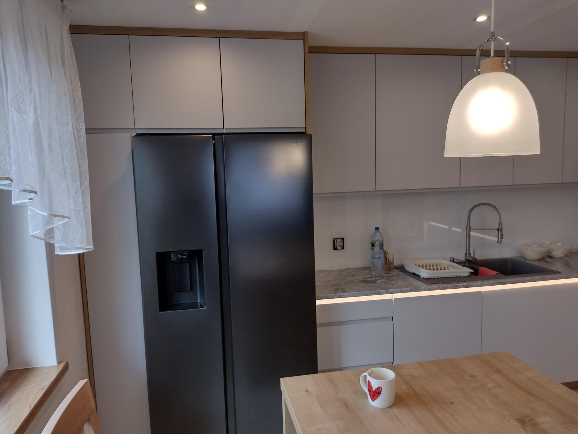 Centralny element, jakim jest wyspa kuchenna z jasnego drewna, tworzy naturalny kontrast i zapewnia dodatkową przestrzeń roboczą.